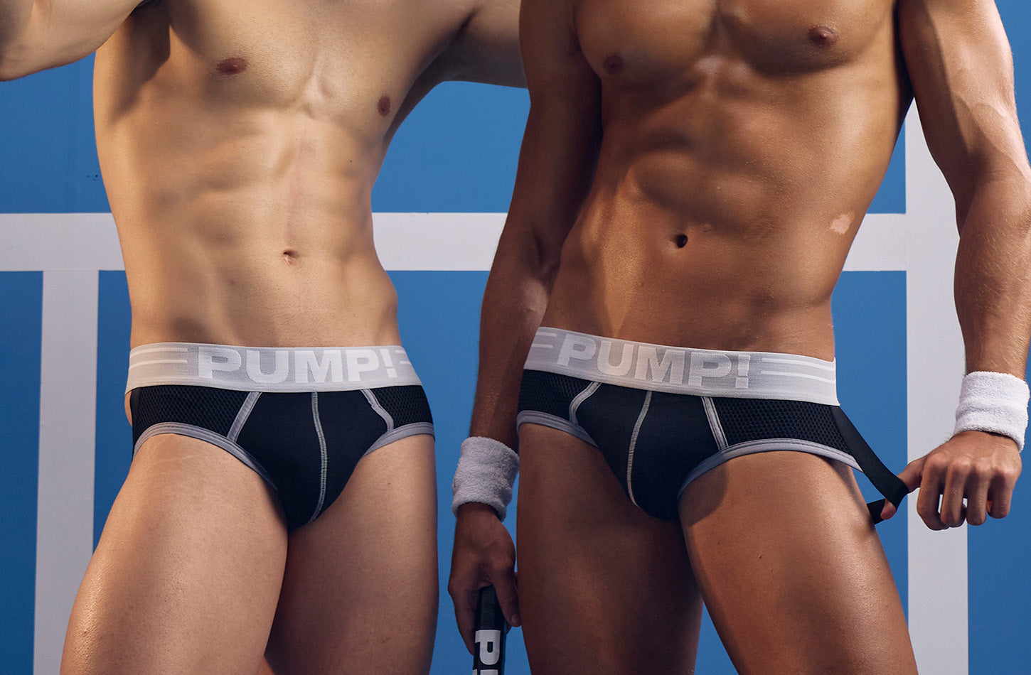 Two models wearing black PUMP! Courtside Full Front Jockstraps on a blue court